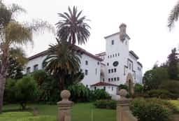 White stucco Santa Barbara County Courthouse with its clock tower behind tall palm trees and a lawn
