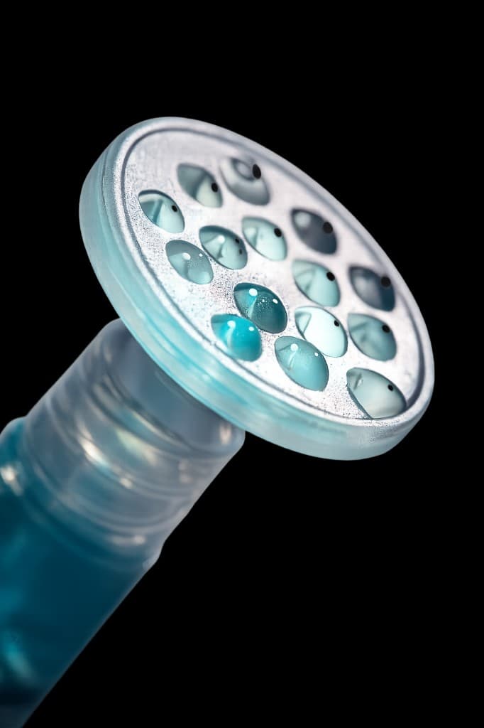 Macro close-up of the CuraCator applicator head showing multiple dispensing channels filled with teal biologic fluid
