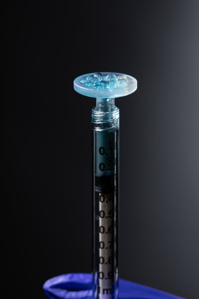 CuraCator syringe loaded with teal PRP biologic preparation, viewed from above against dark background