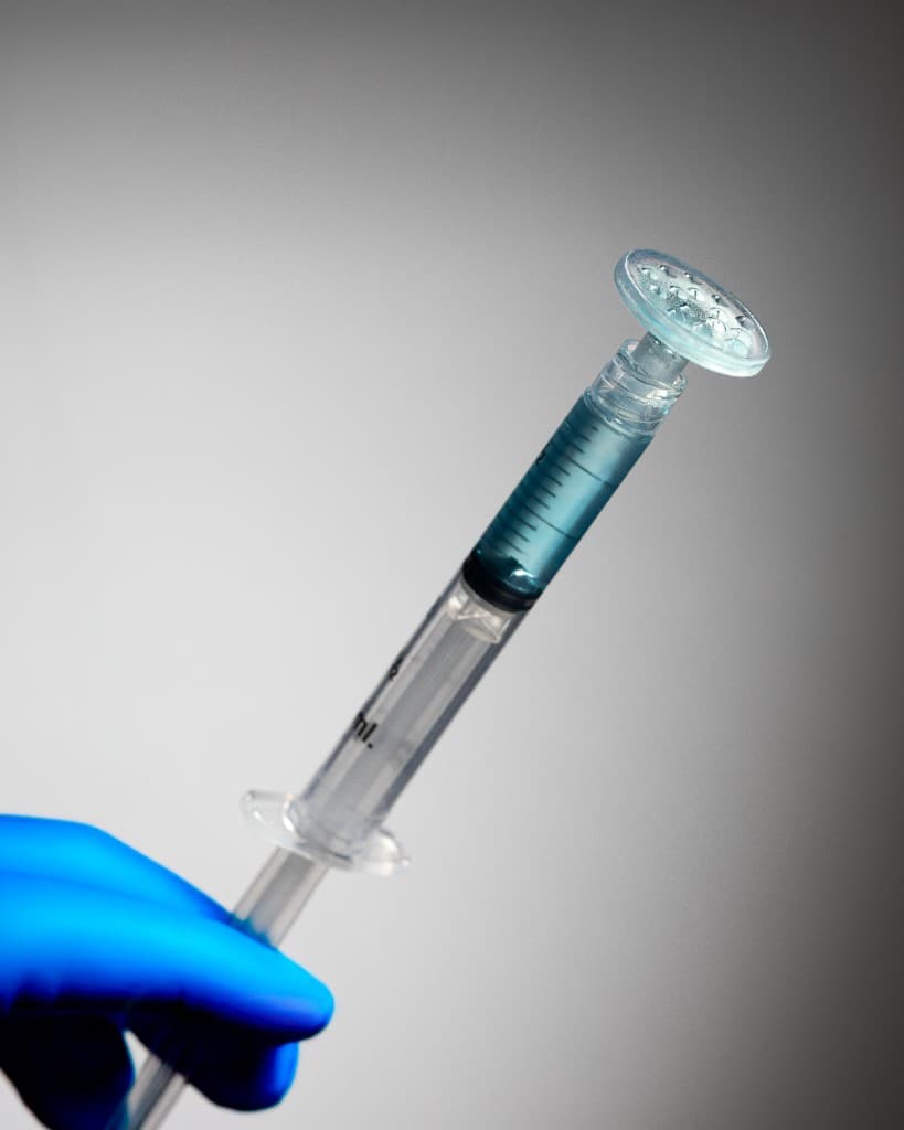 Gloved hand holding a CuraCator-compatible syringe with biologic solution