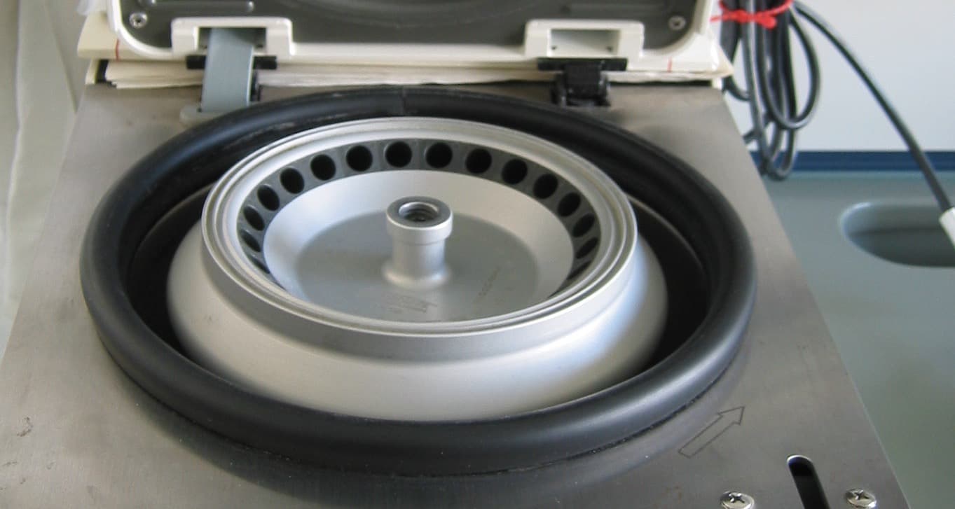 Open benchtop centrifuge showing a round fixed-angle rotor with a ring of tube holes inside a rubber-sealed chamber