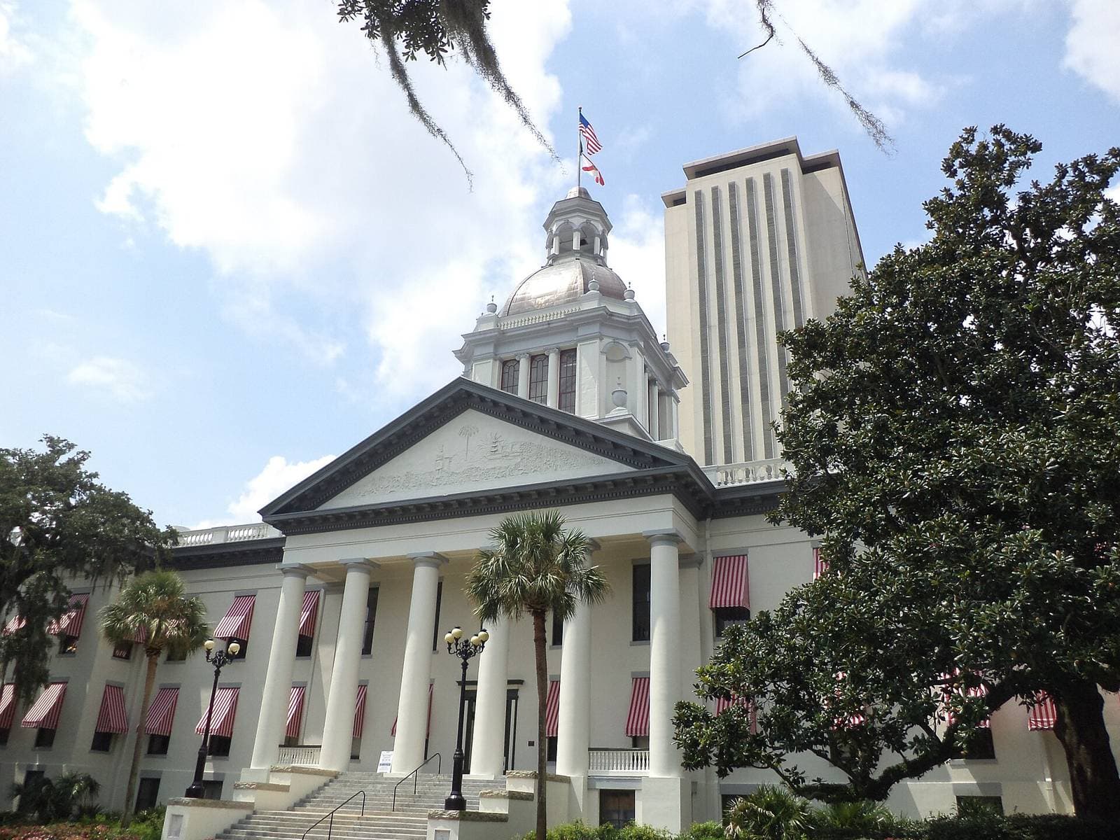 Florida Historic Capitol with white columns and red striped awnings in front of the high-rise Florida State Capitol tower in Tallahassee