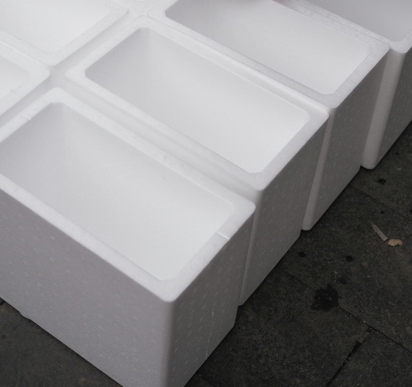 Rows of open white expanded polystyrene shipping boxes on a dark paved floor
