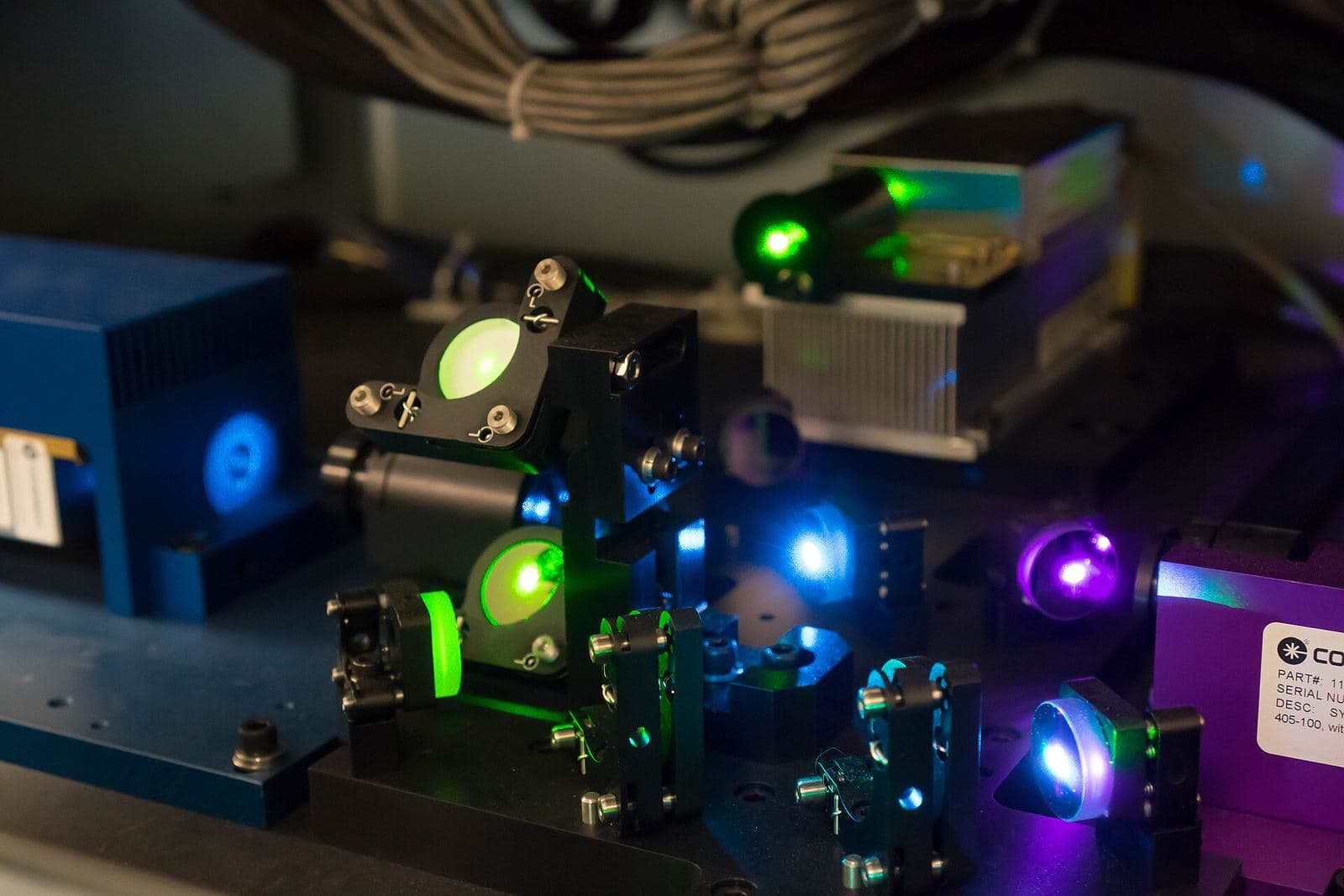 Lasers, lenses and filters glowing green, blue and violet on the optical bench inside a research flow cytometer