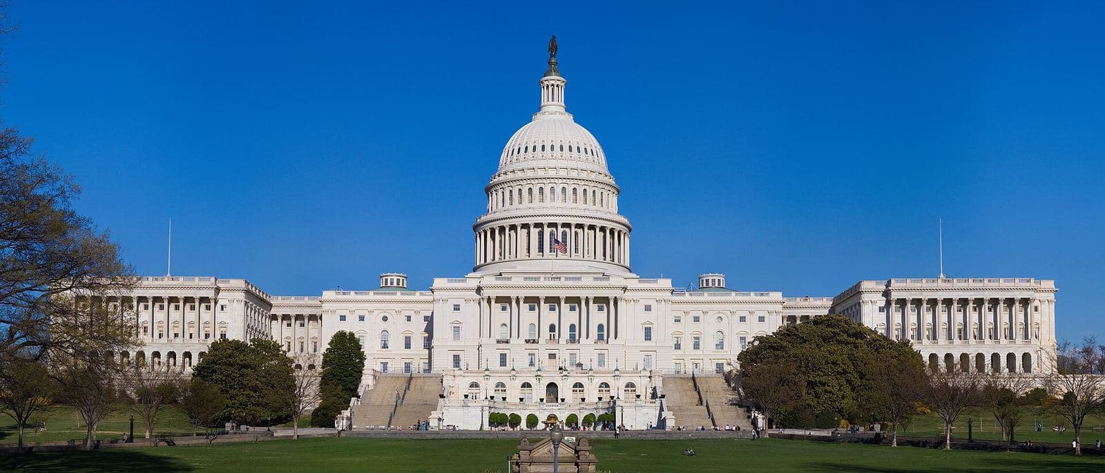 The west front of the United States Capitol with its dome, under a clear blue sky, seen across a lawn