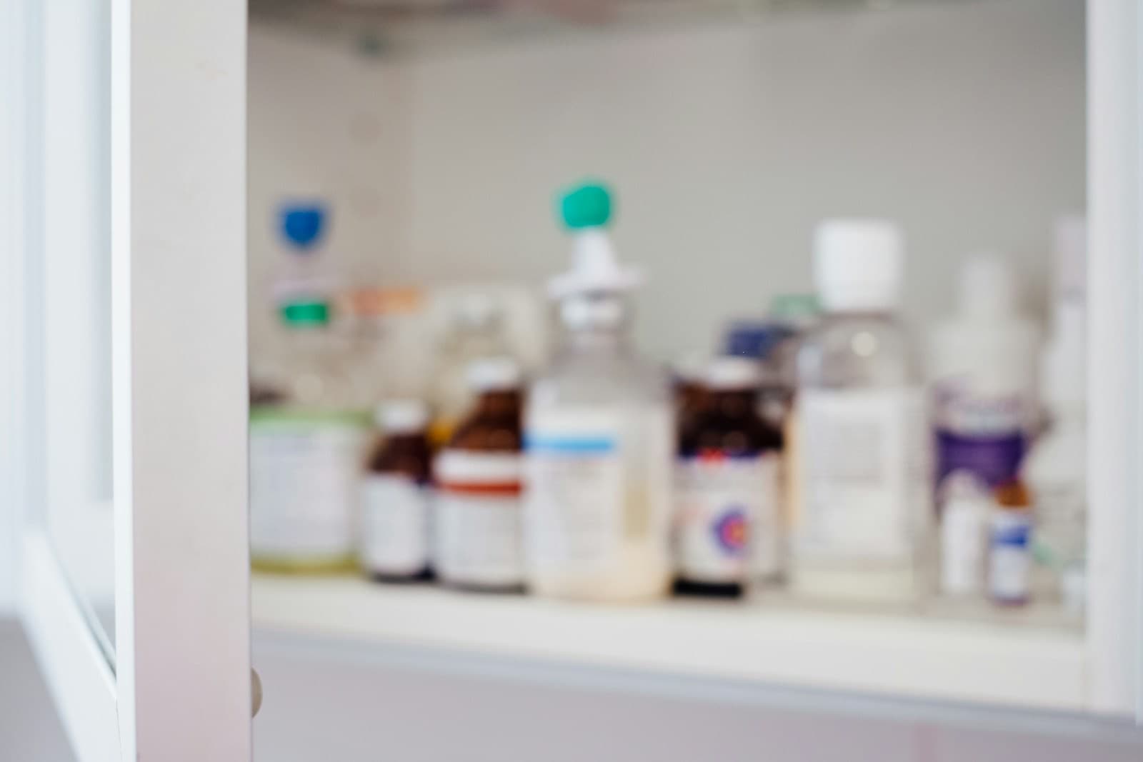 Out-of-focus pharmacy shelf holding assorted bottles and containers behind a glass cabinet door