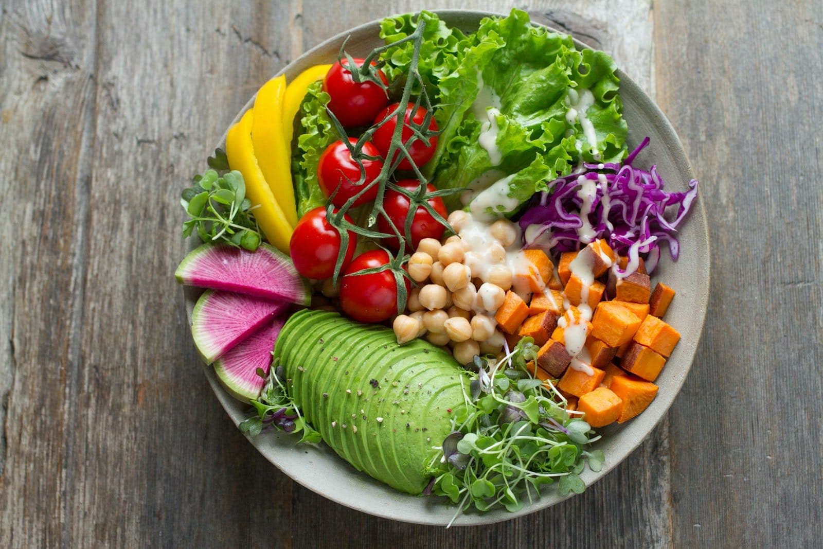 Overhead view of a bowl with lettuce, tomatoes, chickpeas, sweet potato, avocado, red cabbage and radish on a wooden table