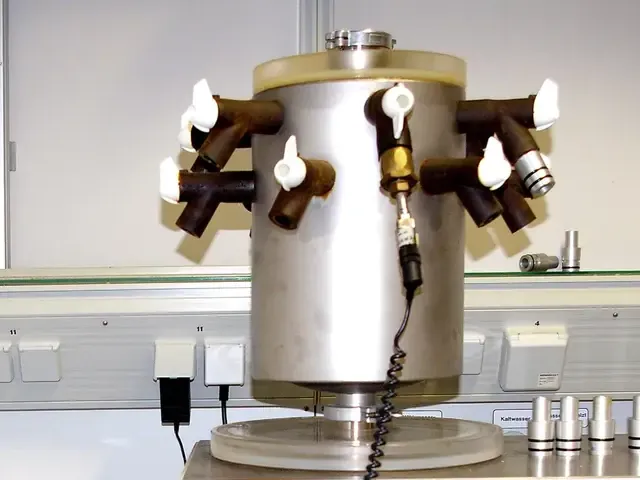 The drying chamber of a benchtop laboratory freeze-dryer: a stainless steel cylinder with valved sample ports, seated on a clear plate above the condenser unit
