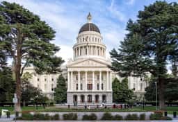 California State Capitol dome and columned front in Sacramento, framed by large trees